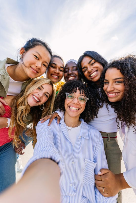 Diverse group of happy young best female friends having fun together outdoors. International youth community concept with multiracial girls from different cultures smiling at camera.